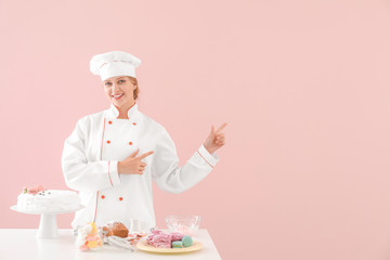 Poster - Female confectioner with tasty desserts on color background