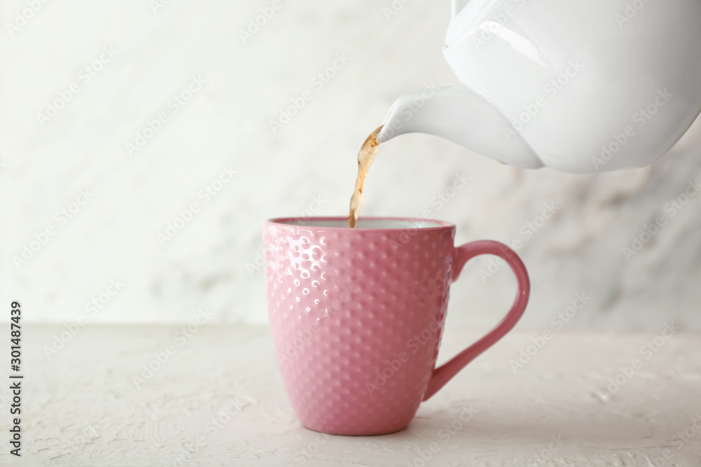 Pouring of hot tea from teapot into cup on table - obrazy, fototapety, plakaty 