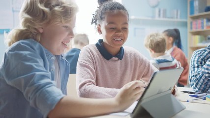Wall Mural - in the elementary school: girl and a boy work as a team using tablet computer. diverse classroom wit