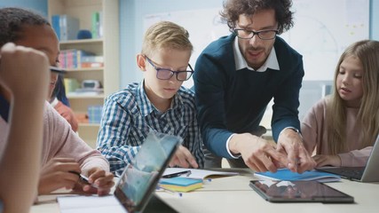 Wall Mural - elementary school classroom: enthusiastic teacher holding tablet computer explains lesson to brillia