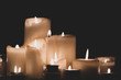 Composition of burning candles close-up on a dark background. Melted wax candles of different shapes.