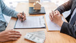© Pichsakul - Businessman signs contract behind home architectural model Discussion with a real estate agent rental company staff  at the office property appraisal and valuation concept.