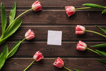 Wall Mural - blank greeting card with pink tulips and an empty sticker on a wooden table