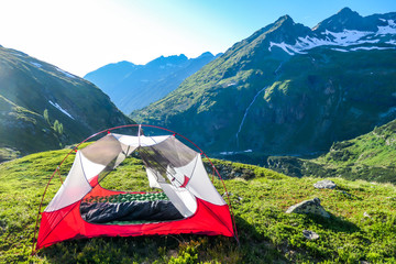an unfolded tent on a meadow in high alps. slopes of the mountains partially covered with snow. wild