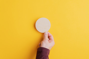 Male hand placing blank wooden cut circle on yellow background