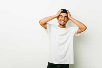 Wall Mural - Young hispanic man laughs joyfully keeping hands on head. Happiness concept.