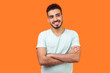 © khosrork - Portrait of dreamy thoughtful bearded man with toothy smile in white t-shirt standing with crossed hands, dreaming and thinking of pleasant memories. indoor studio shot isolated on orange background