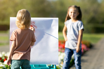 Brother and sister paint funny portraits of people with paints paper. Children paint portraits of each other on the street.