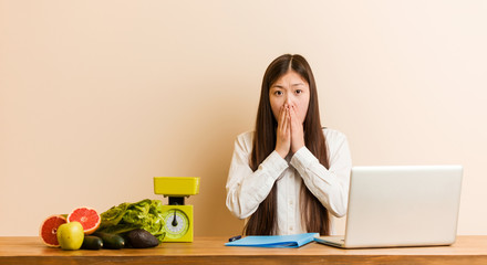 Wall Mural - Young nutritionist chinese woman working with her laptop scared and afraid.