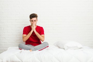 Wall Mural - Young teenager student man on the bed holding hands in pray near mouth, feels confident.