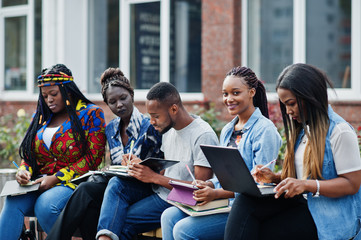 Wall Mural - Group of five african college students spending time together on campus at university yard. Black afro friends studying at bench with school items, laptops notebooks.