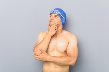 Wall Mural - Young professional swimmer man looking sideways with doubtful and skeptical expression.