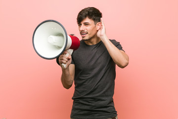 Wall Mural - Young hispanic man holding a megaphone trying to listening a gossip.