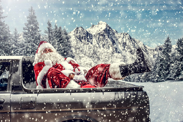 Wall Mural - Bearded in red clothes sits on the back of a white truck.Santa distributes gifts for children.Landscape of mountains and winter forest covered with snow and frost.Christmas time.Copy space.Snowflakes 