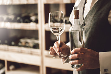 Wall Mural - Sommelier Concept. Senior man standing with bottle and glass of white wine close-up