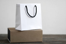 White Paper Bag And Craft Gift Box On Wooden Table. Brand Packaging Concept. Copy Space For Text