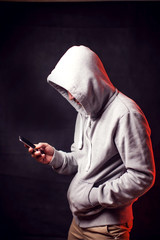 Man wearing hoody sweater with phone in hands. Crime and hacking concept