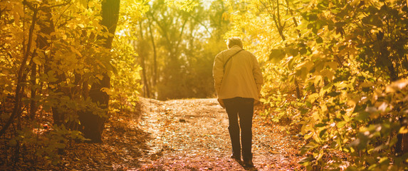 lonely senior man walking in the autumn forest with fallen leaves, sadness concept