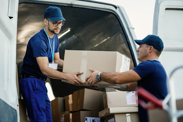 Wall Mural - Young couriers cooperating while unloading packages from delivery van.