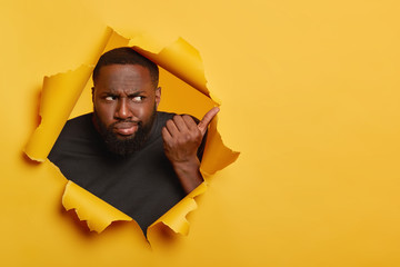 Now way, bad choice. Photo of frustrated unhappy black man smirks face, points away with unimpressed suspicious look, poses in ripped yellow paper background, disappointed by something unpleasant