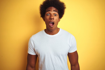 Poster - American man with afro hair wearing white t-shirt standing over isolated yellow background afraid and shocked with surprise expression, fear and excited face.