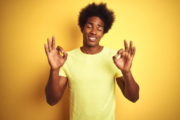 Sticker - African american man with afro hair wearing t-shirt standing over isolated yellow background relax and smiling with eyes closed doing meditation gesture with fingers. Yoga concept.