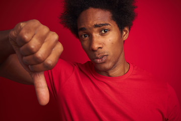 Sticker - Young american man with afro hair wearing t-shirt standing over isolated red background with angry face, negative sign showing dislike with thumbs down, rejection concept