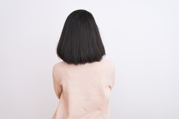 Wall Mural - Young chinese woman wearing turtleneck sweater standing over isolated white background standing backwards looking away with crossed arms