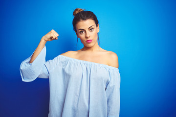 Canvas Print - Young beautiful woman wearing bun hairstyle over blue isolated background Strong person showing arm muscle, confident and proud of power