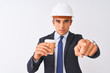 © Krakenimages.com - Young handsome architect man wearing helmet drinking coffee over isolated white background pointing with finger to the camera and to you, hand sign, positive and confident gesture from the front