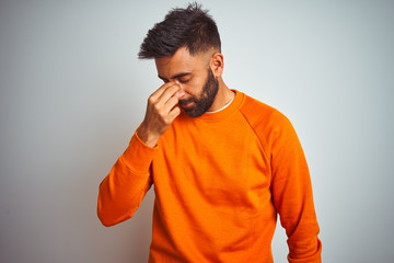 Poster - Young indian man wearing orange sweater over isolated white background tired rubbing nose and eyes feeling fatigue and headache. Stress and frustration concept.