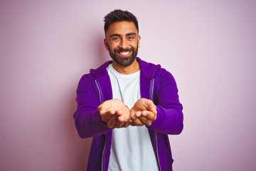 Sticker - Young indian man wearing purple sweatshirt standing over isolated pink background Smiling with hands palms together receiving or giving gesture. Hold and protection