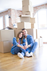 Poster - Young beautiful couple in love moving to new home, sitting on the floor very happy and cheerful for new apartment around cardboard boxes