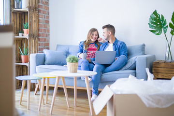 Poster - Young couple relaxing sitting on the sofa using the computer laptop around cardboard boxes, very happy moving to a new house