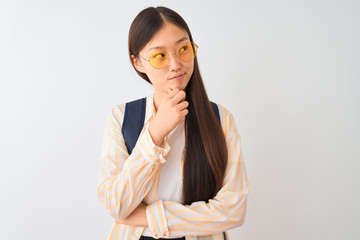 Sticker - Young chinese student woman wearing glasses and backpack over isolated white background with hand on chin thinking about question, pensive expression. Smiling with thoughtful face. Doubt concept.