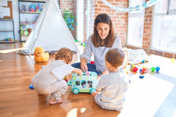 Wall Mural - Beautiful teacher and toddlers playing around lots of toys at kindergarten