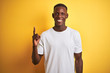 © Krakenimages.com - Young african american man wearing white t-shirt standing over isolated yellow background showing and pointing up with finger number one while smiling confident and happy.