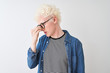 © Krakenimages.com - Young albino blond man wearing denim shirt and glasses over isolated white background tired rubbing nose and eyes feeling fatigue and headache. Stress and frustration concept.