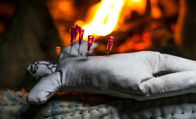 black magic doll sleeping in the darkness and lots of needles dipped into it's chest and bonfire in the background  