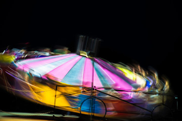 Amusement park ride fast spinning carousel roundabout with motion blur. Fun fair carnival  rides at fairground. Family vacation, leisure and recreation concept