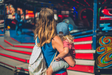 Wall Mural - Young mother carrying her toddler at a funfair