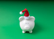 Piggy bank in a Santa Claus hat on a green background. Concept for Christmas holiday debt and expenses