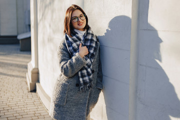 Wall Mural - Attractive young girl wearing glasses in a coat walking on a sunny day