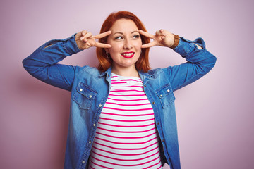 Sticker - Beautiful redhead woman wearing denim shirt and striped t-shirt over isolated pink background Doing peace symbol with fingers over face, smiling cheerful showing victory