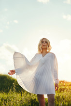 Girl In A Long White Dress Dancing In The Field. Blonde Woman In The Sun In A Light Dress. Girl Resting And Dreaming, Perfect Summer Makeup On Her Face