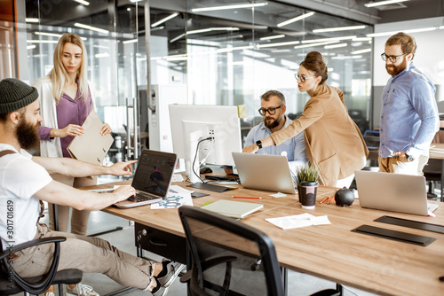 Fototapeta na szkło Grupa różnorodnych kolegów pracujących na komputerach w nowoczesnej przestrzeni biurowej lub coworkingowej, brodaty hipster jako programista piszący kod