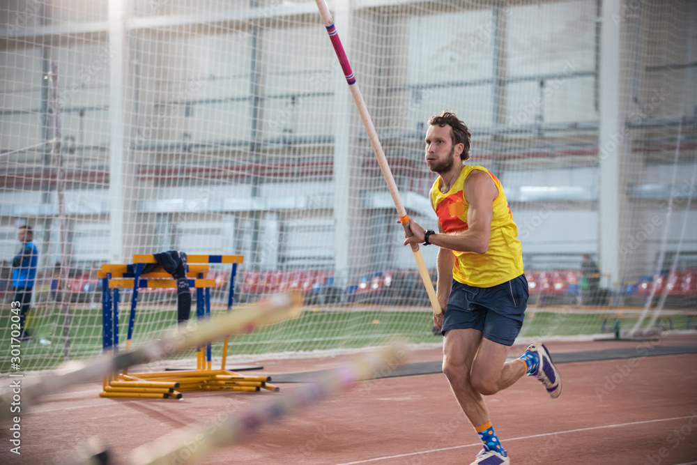 Pole vaulting - man in blue shorts is running with pole in hands - obrazy, fototapety, plakaty 