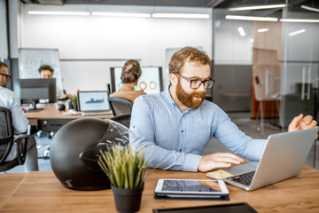 Wall Mural - young man dressed casually working on the laptop in the office with coworkers on the background