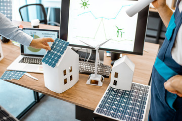 Wall Mural - People working on a project of alternative energy, working with house model and computer in the office, close-up on the working place