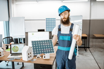 Wall Mural - Portrait of a dedicated worker in workwear with blueprints and solar panel at the alternative energy design office